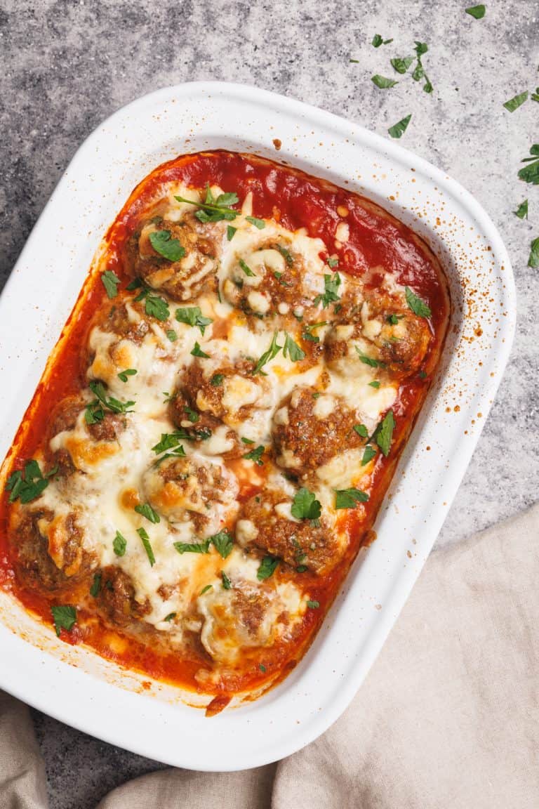 Baked meatballs in a white casserole dish next to a linen tea towel.