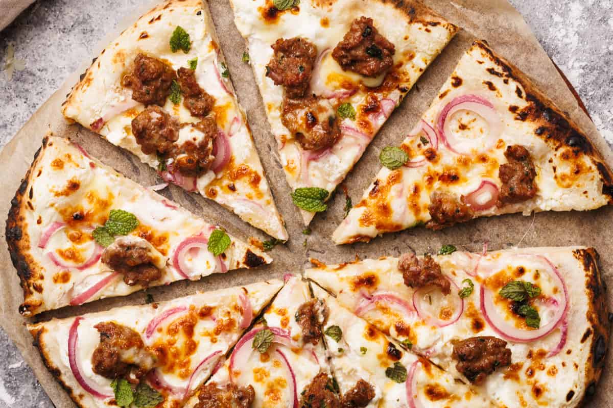 Sliced German pizza on a baking paper lined wooden board next to a linen napkin.