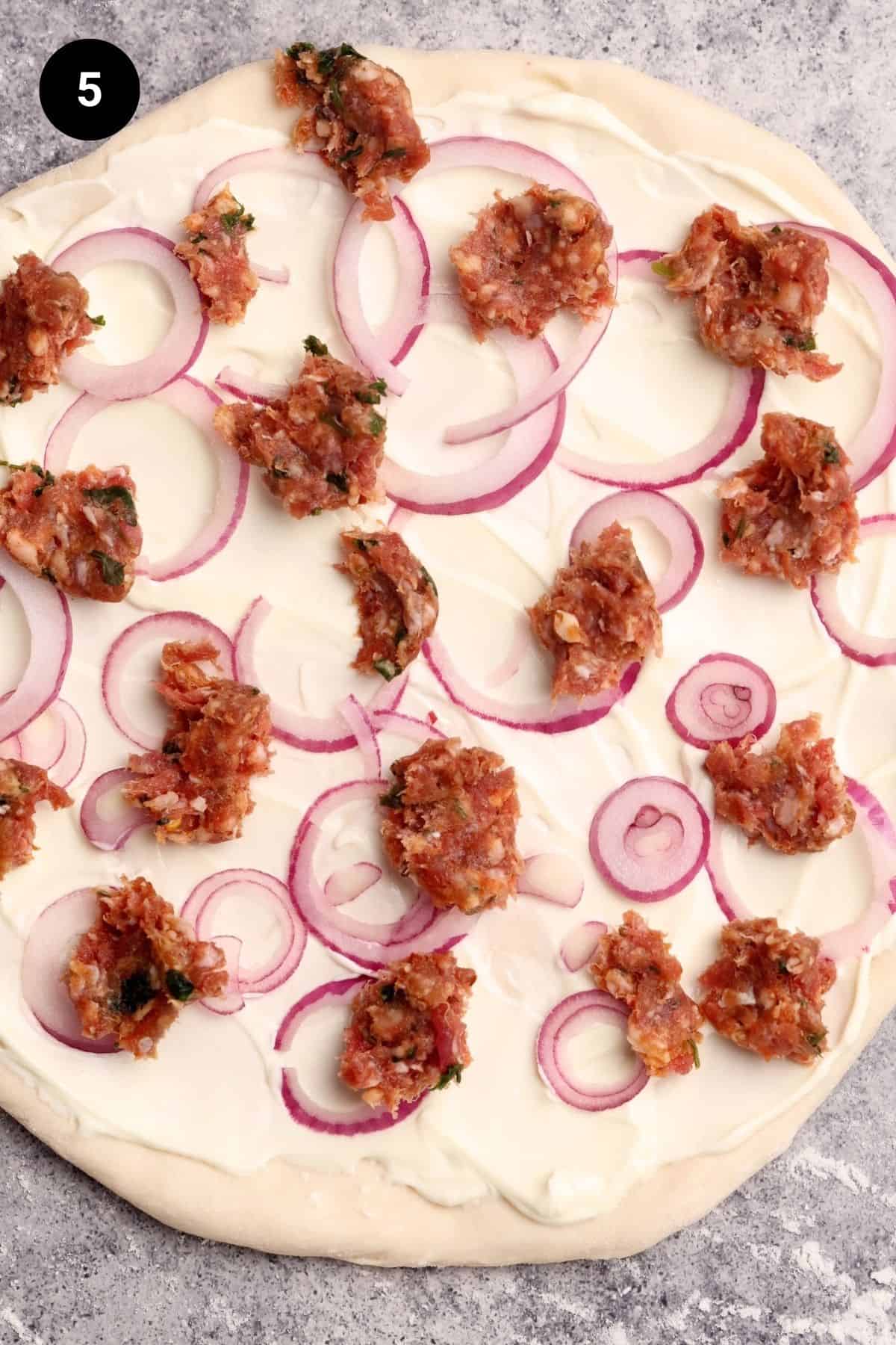 Pizza with sour cream, red onion rings, and uncooked lamb sausage.