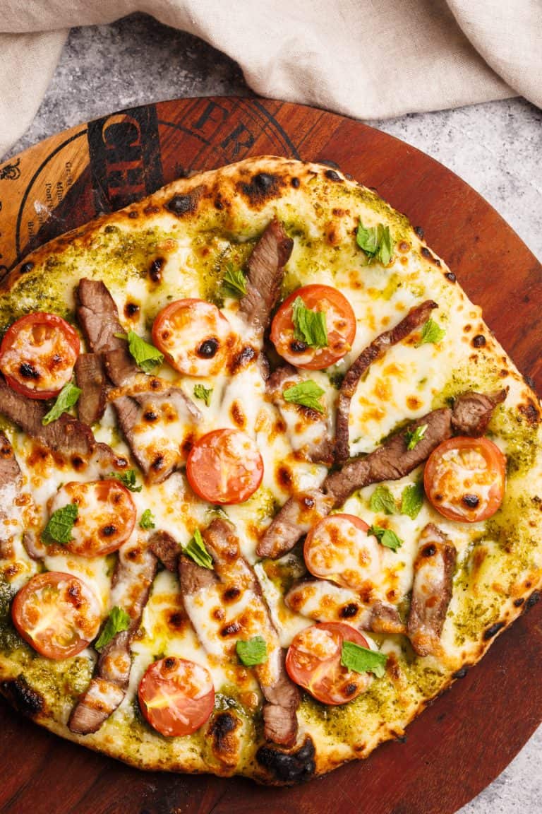 A baked pesto pizza on a wooden board next to a linen napkin.