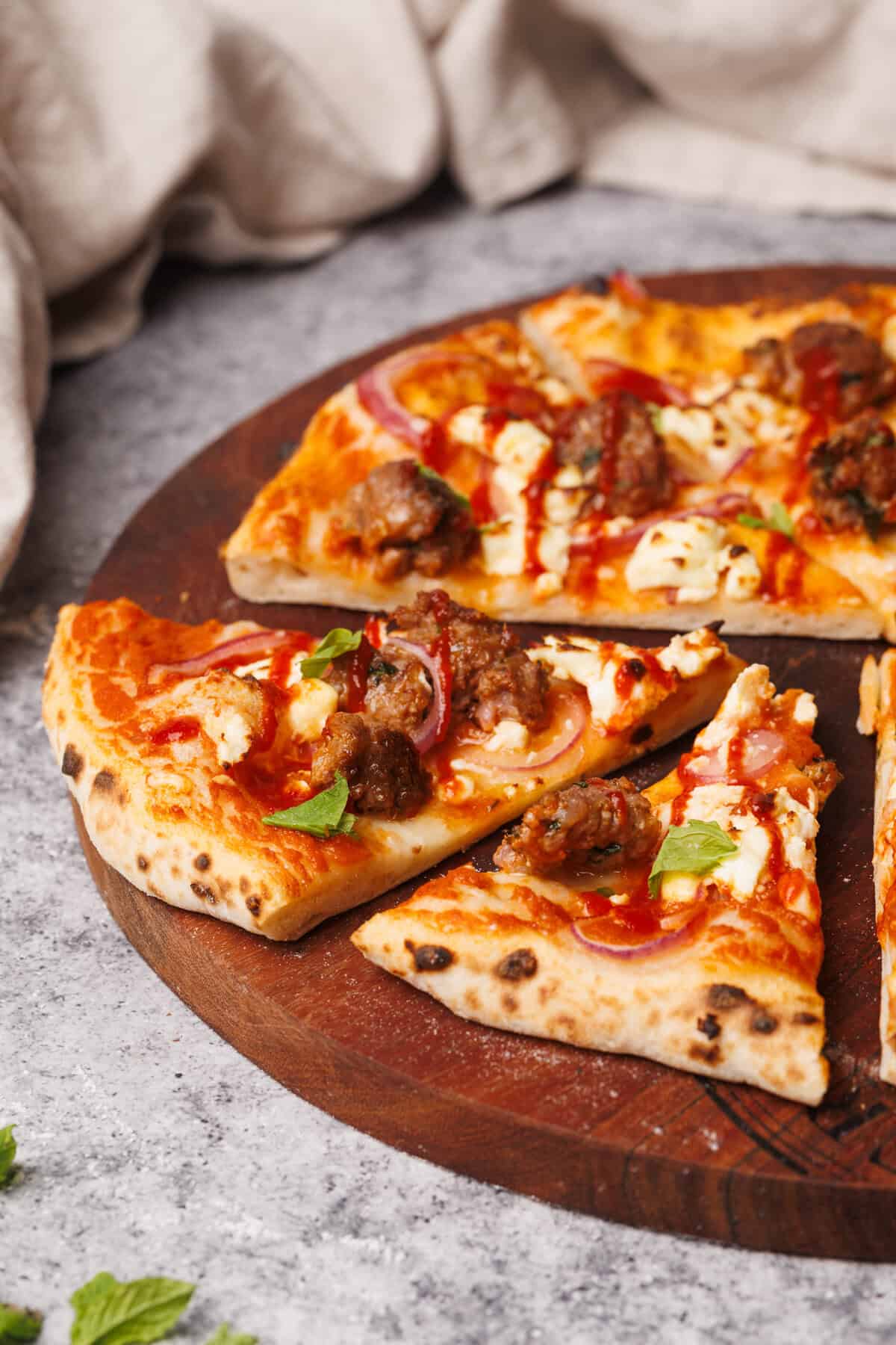 Cut lamb sausage pizza on a round wooden board.