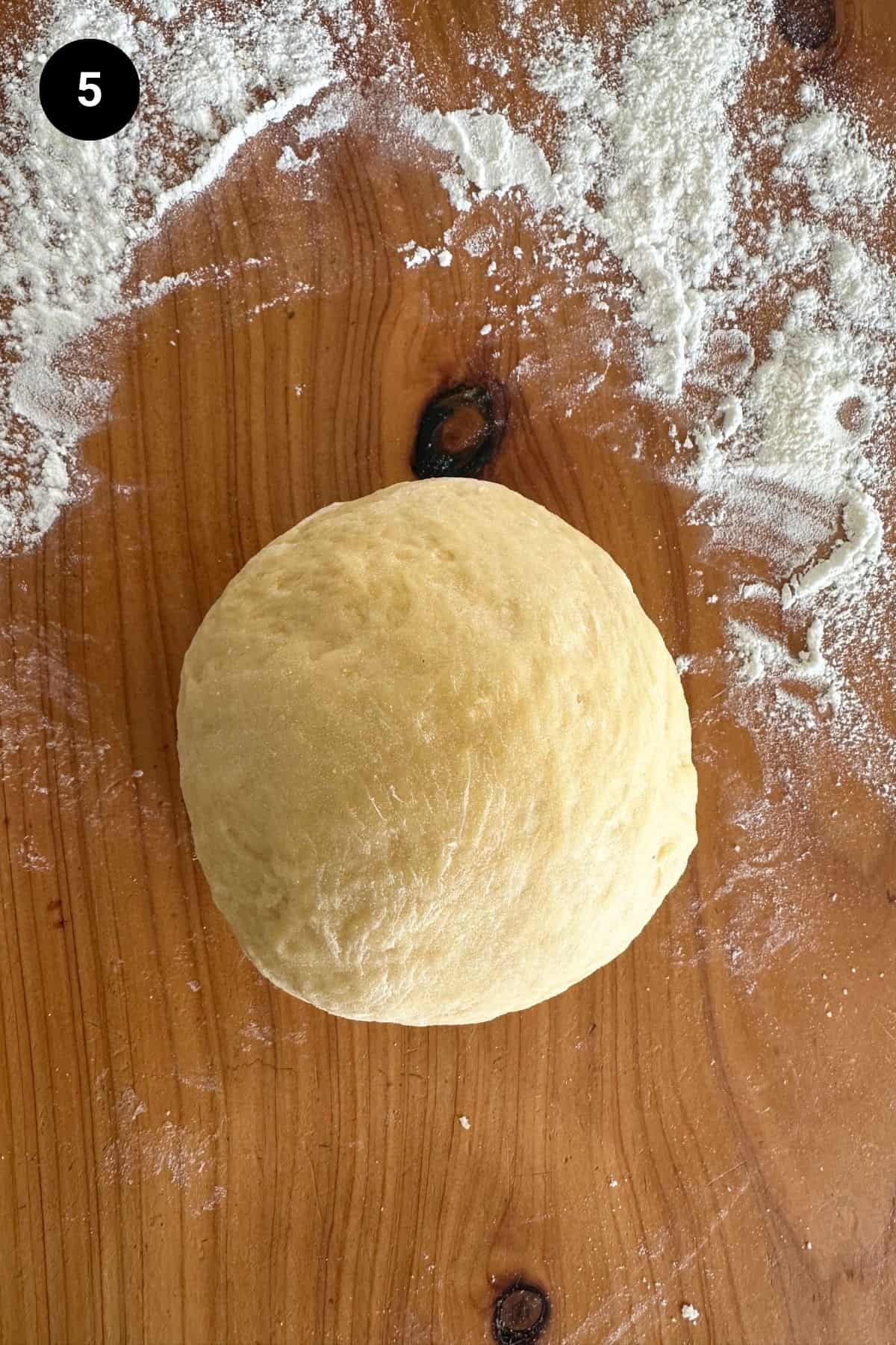 Smooth pasta dough ball on a wooden bench.