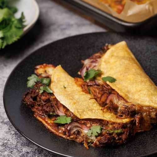 Two baked birria tacos on a black plate.