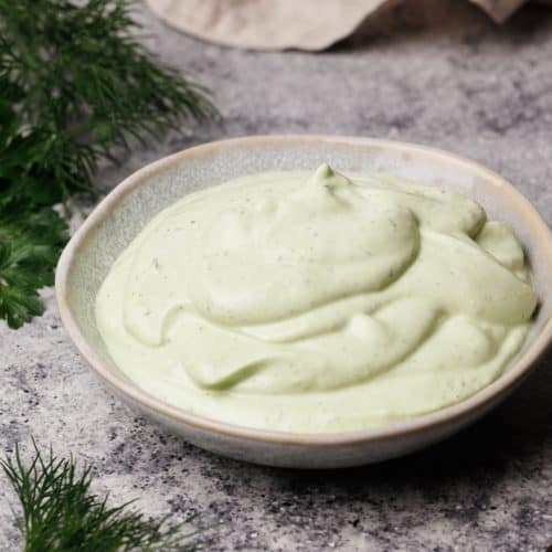 Ranch dip in a small bowl next to fresh herbs and a linen tea towel.