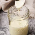 A mason jar with evaporated milk and a spoon spooning it out.