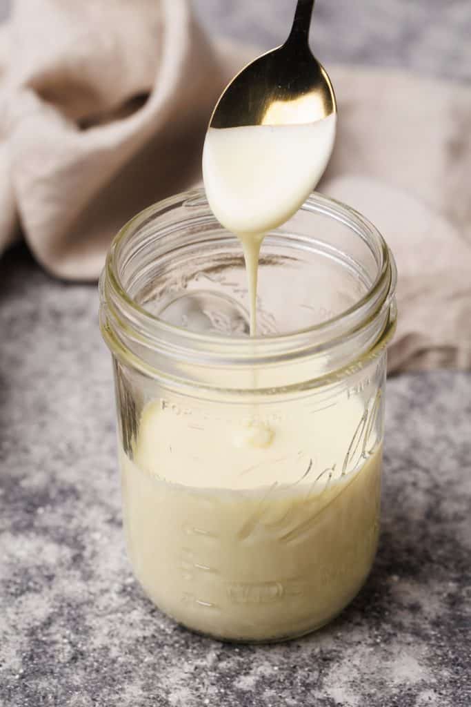 A mason jar with evaporated milk and a spoon spooning it out.