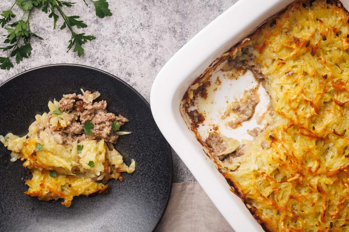 Hash brown beef casserole in a white casserole dish next to a black plate with a portion.
