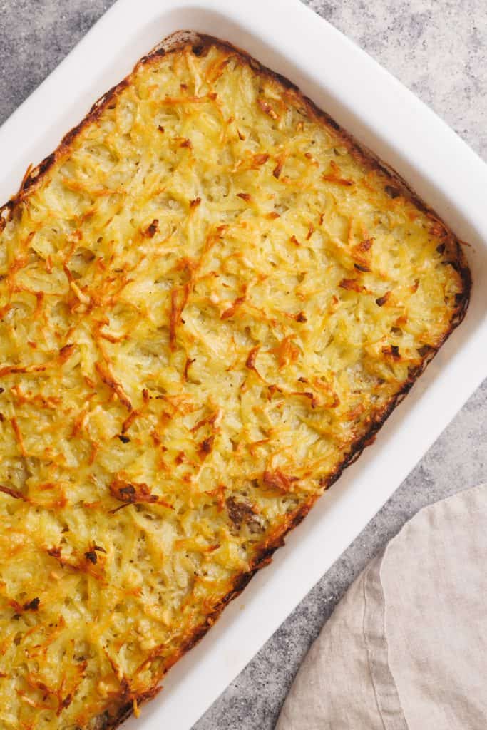 Hash brown beef casserole in a white casserole dish next to a linen towel.