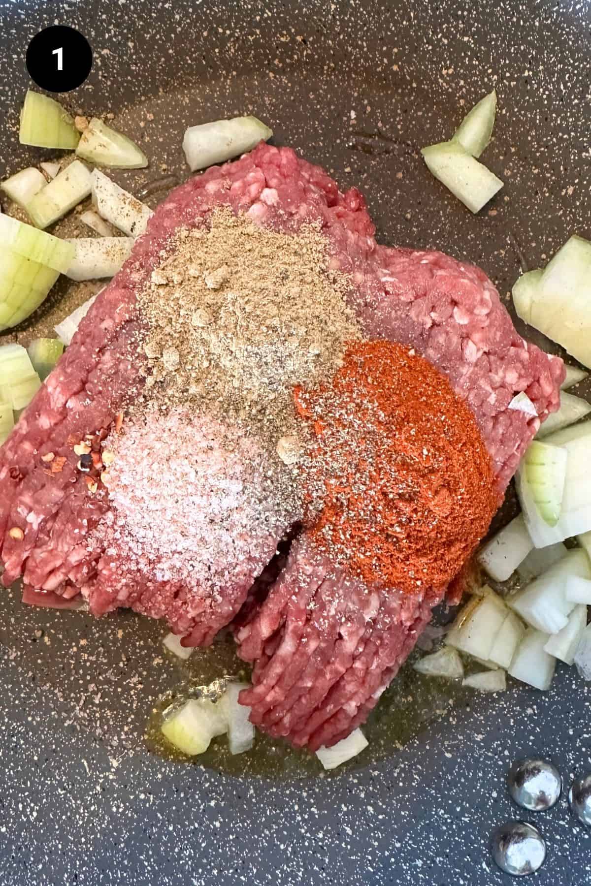 Raw beef with seasonings and onions in a pan.