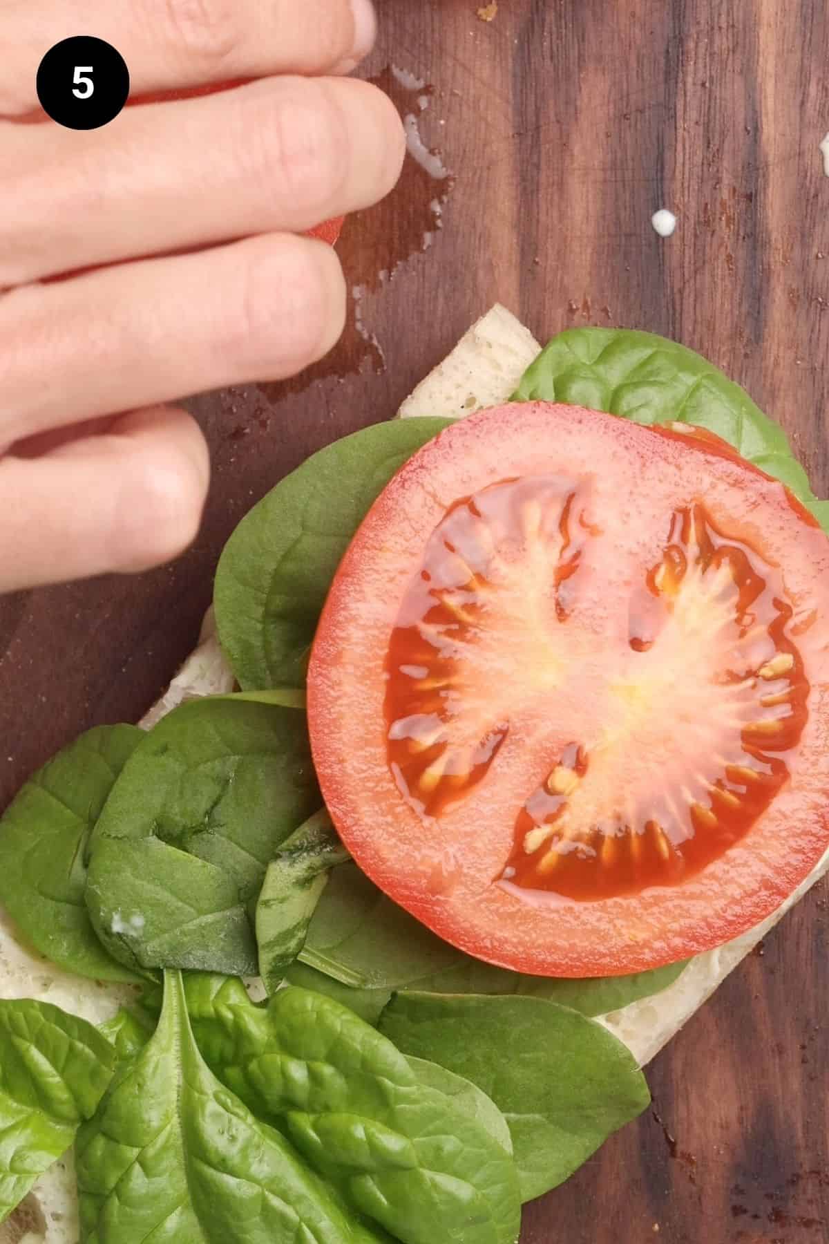 A sandwich being filled with spinach and tomato slices.