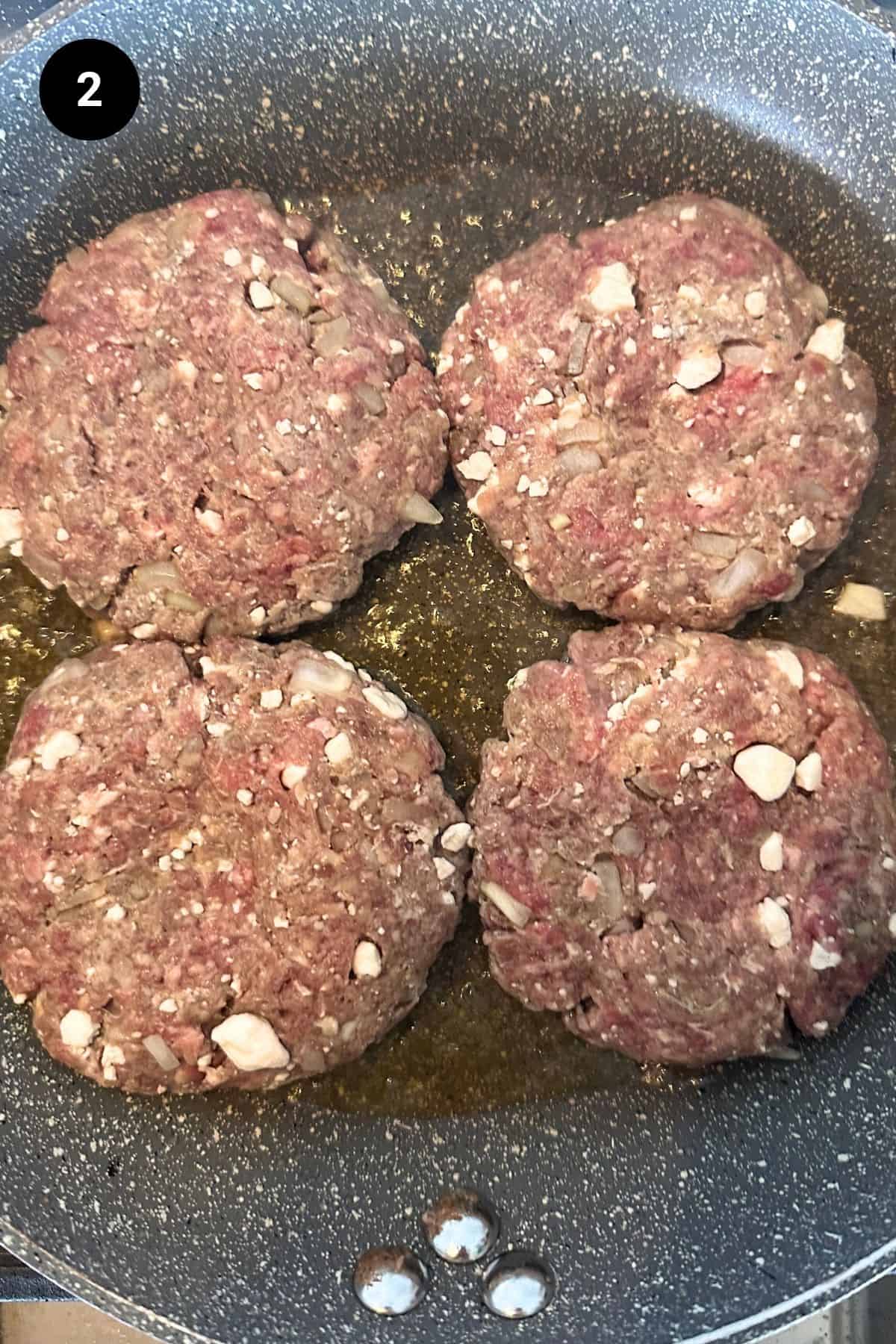 Four hamburger patties being cooked in a pan.