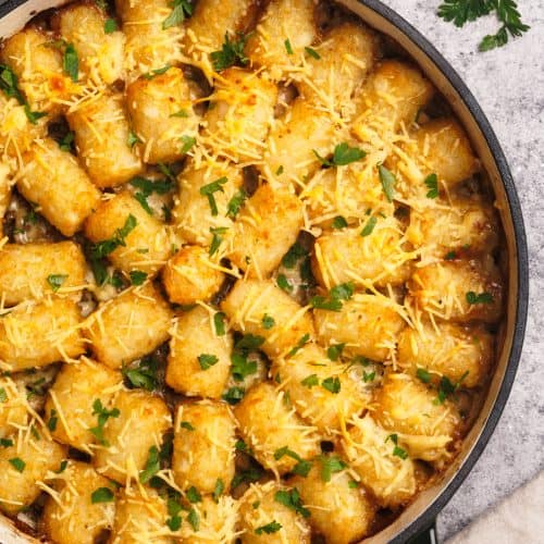 Top down view of the tater tot casserole next to a linen tea towel and fresh parsley.