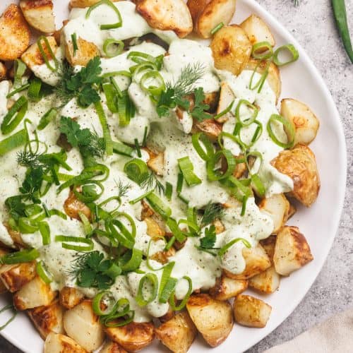 A white plate with loaded ranch potatoes next to a linen tea towel.