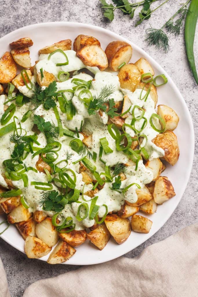A white plate with loaded ranch potatoes next to a linen tea towel.