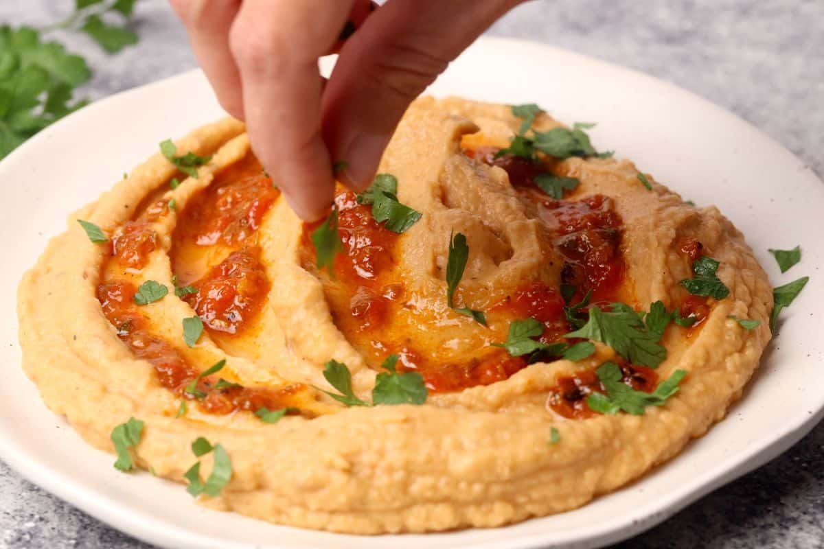 Parsley is being added as garnish to the top of the hummus.