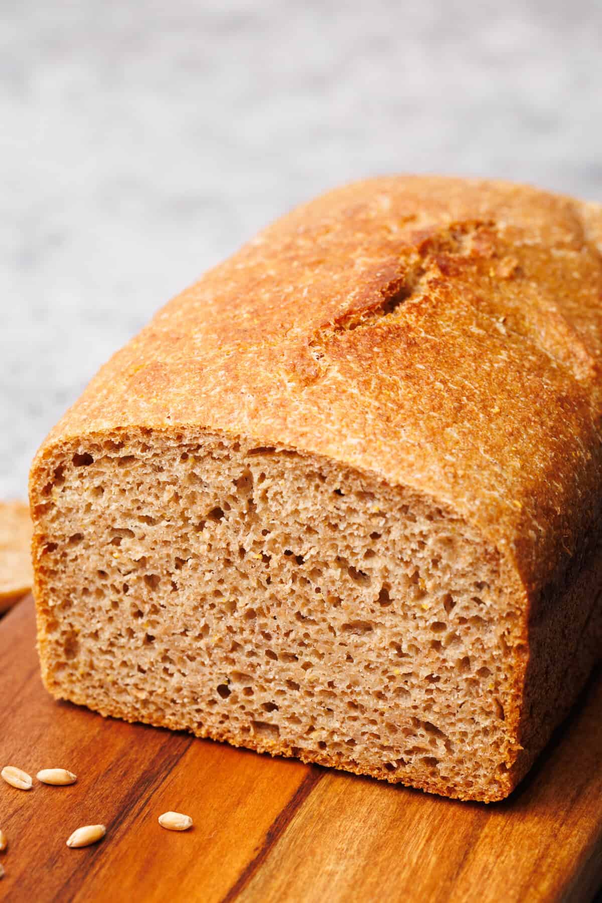A loaf of whole grain spelt bread on a wooden board.