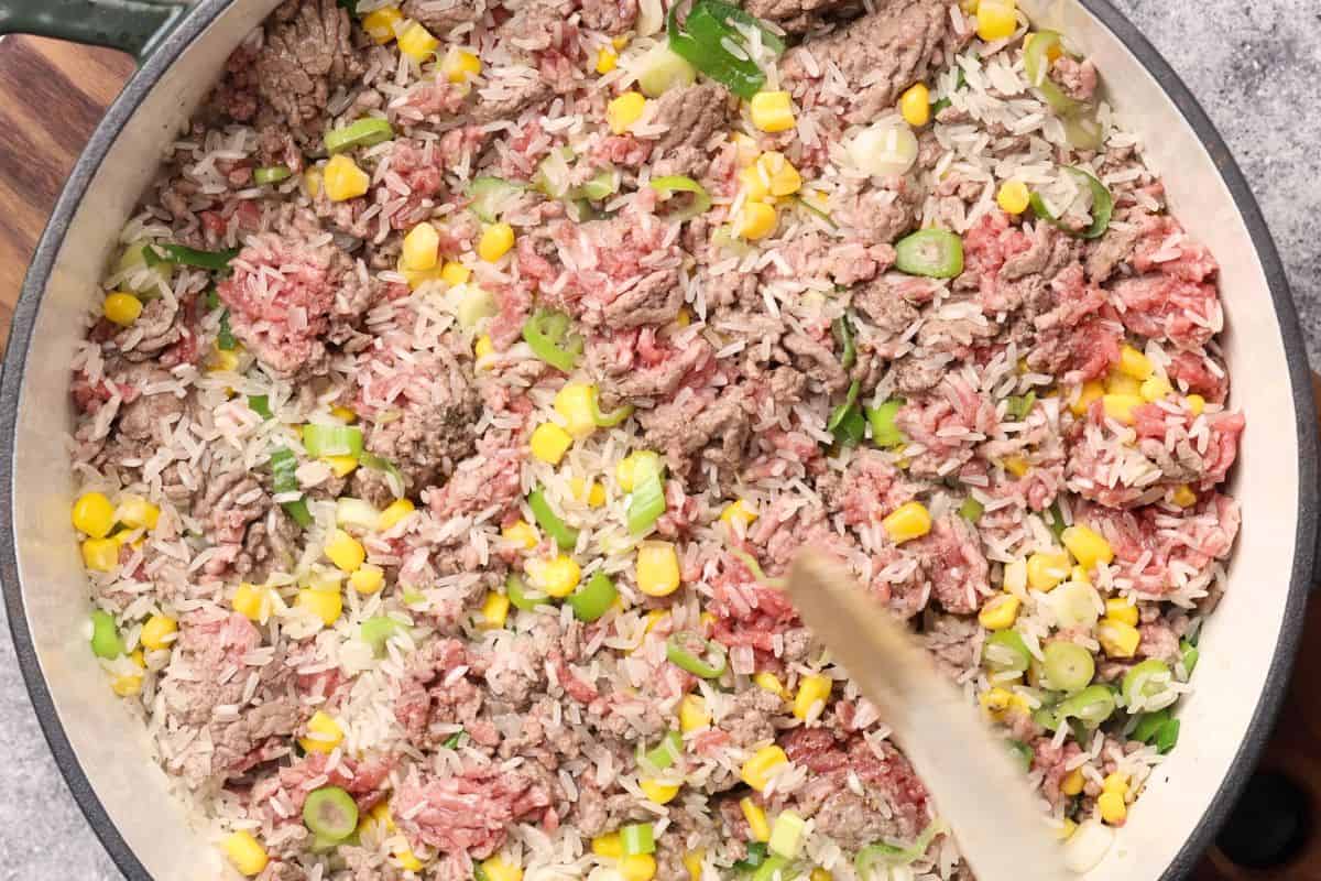 Ground meat and rice mixture with corn and green onions in a skillet.